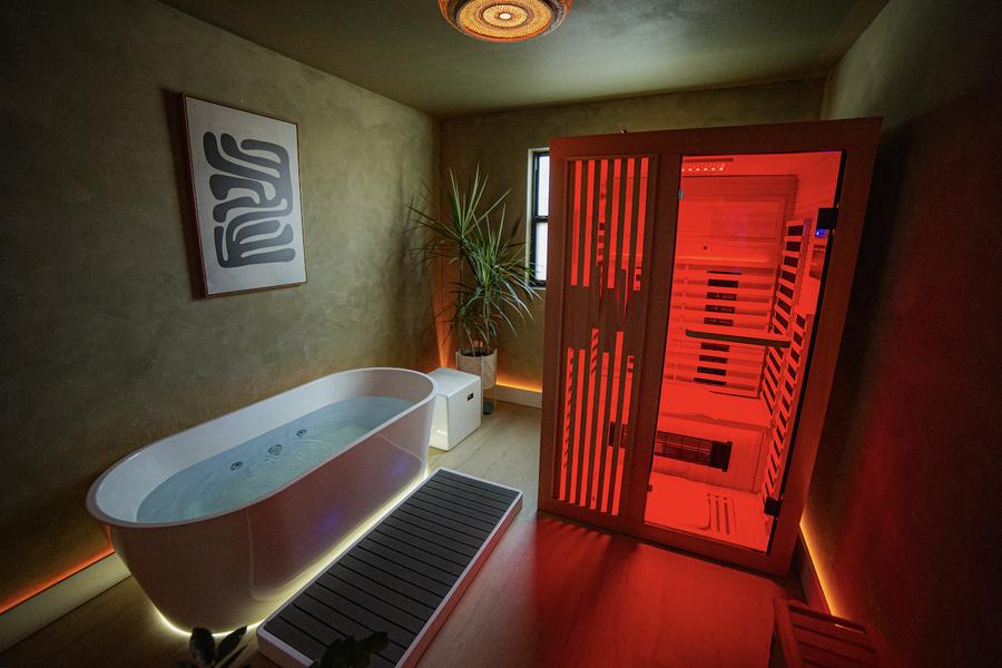 A private suite lit green — infrared sauna and cold plunge tub